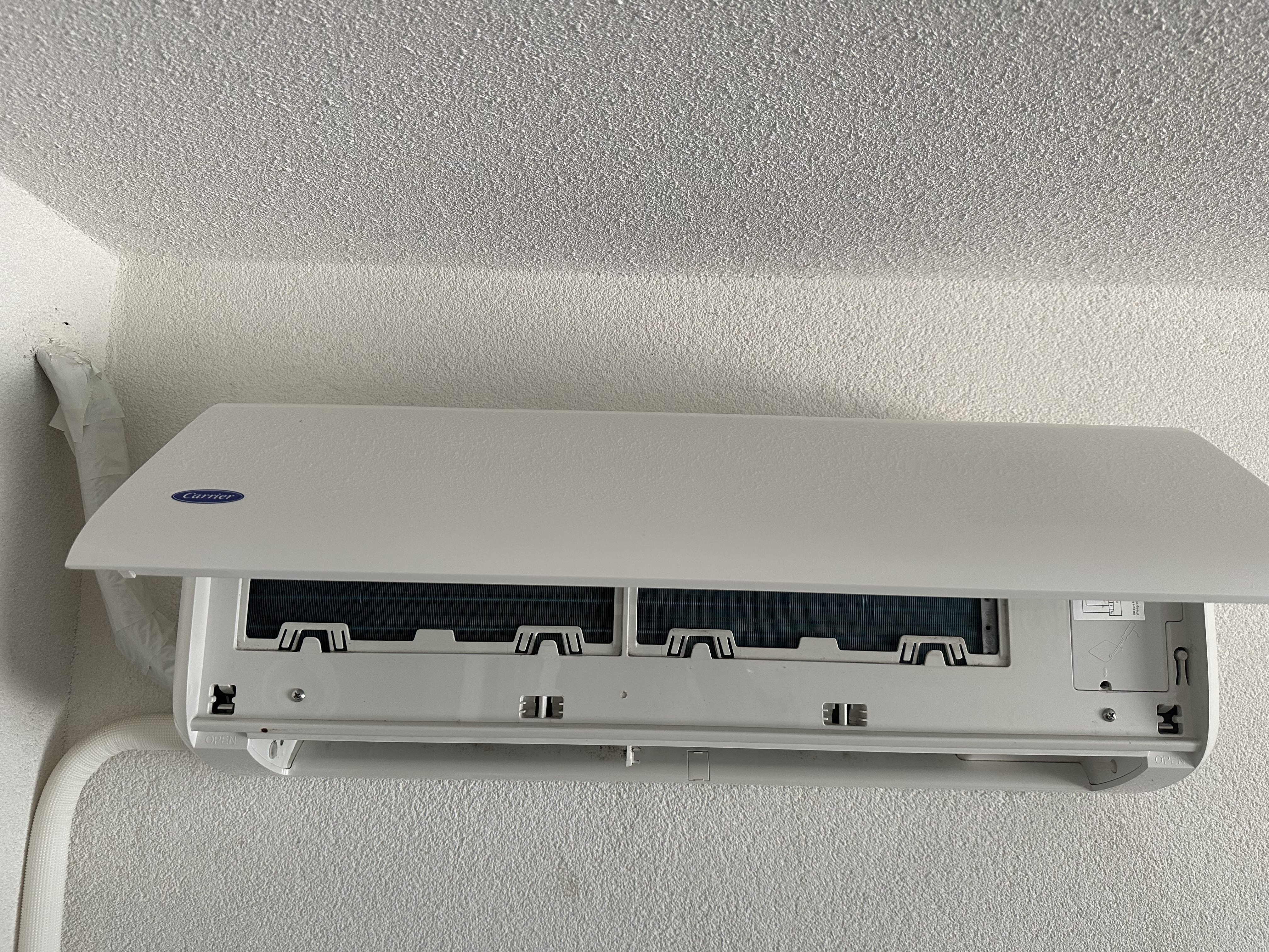 Carrier binnenunit aan witte muur, klepje opengeklapt voor inspectie