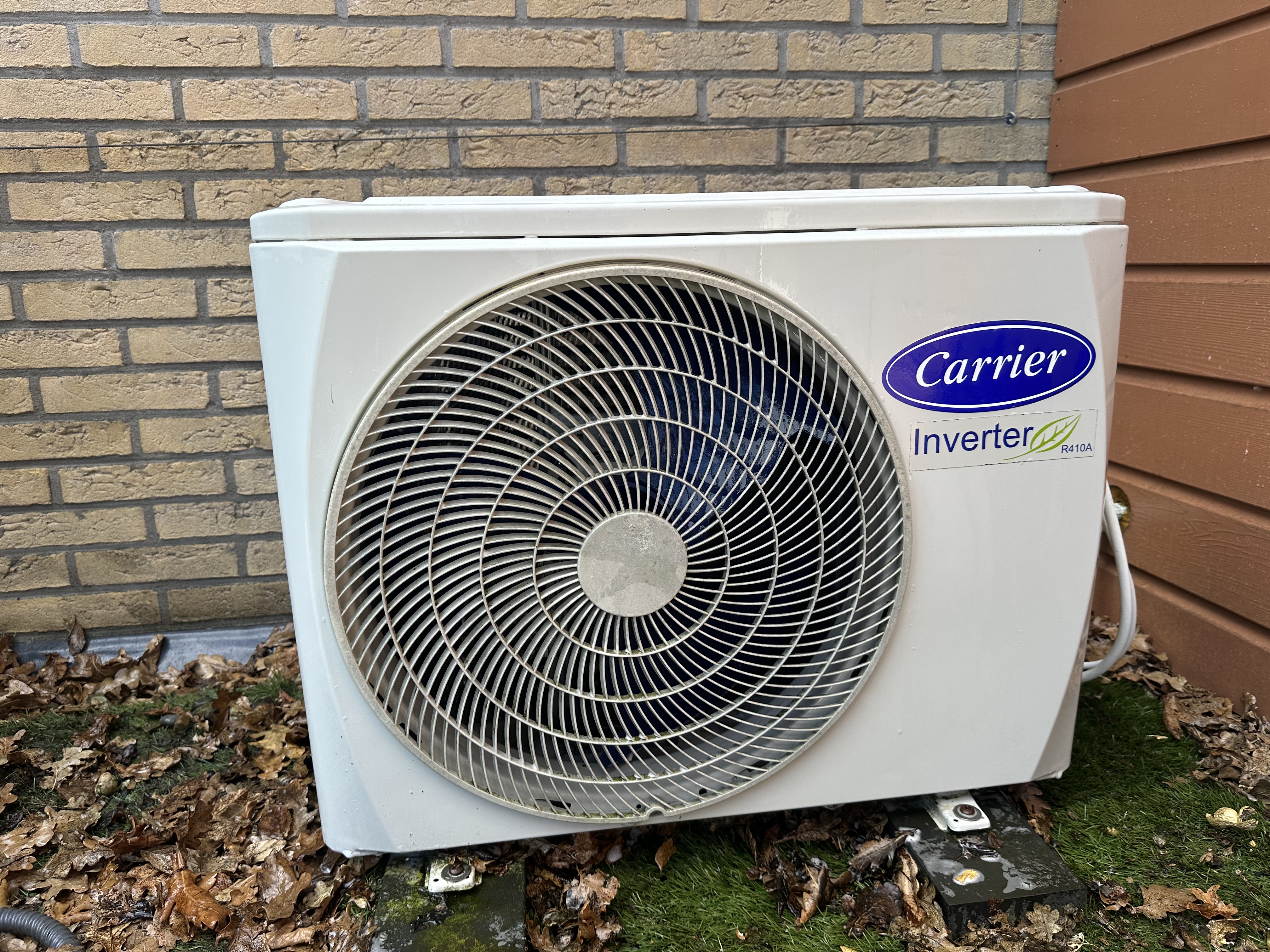 Tweede Carrier buitenunit van de slaapkamer-airco, met bladafval en organische groei eronder vóór reiniging
